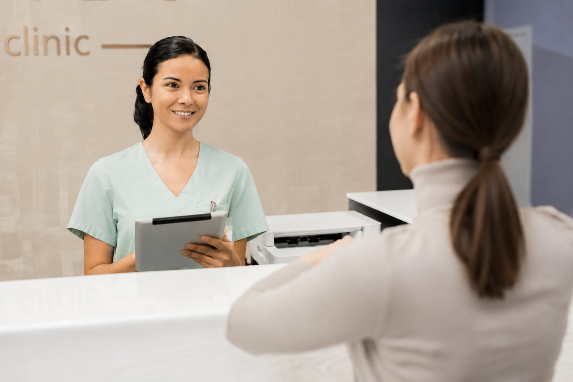 Clinic receptionist holding a tablet while welcoming a client at the front desk